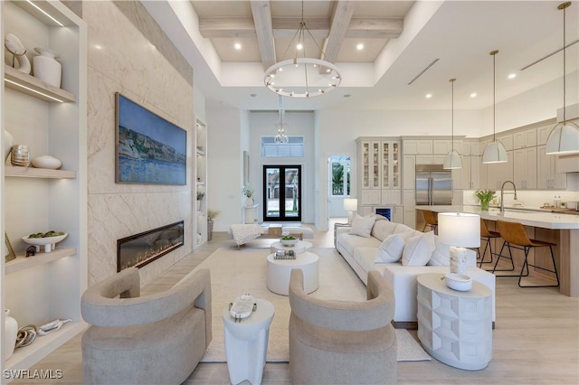 living room with built in shelves, coffered ceiling, a premium fireplace, an inviting chandelier, and light wood-style flooring