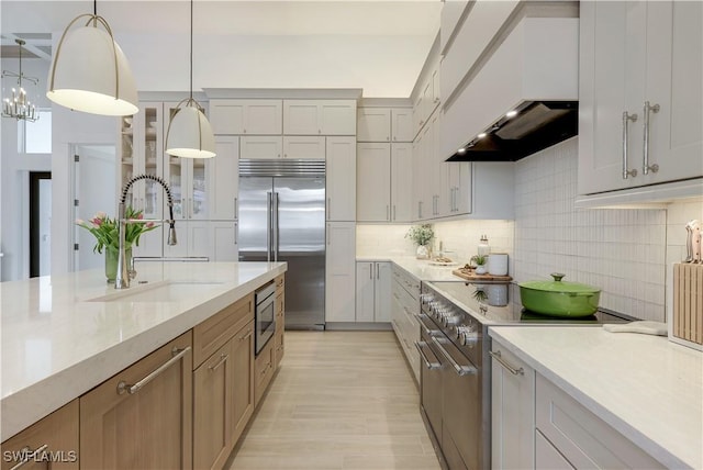 kitchen featuring decorative light fixtures, built in appliances, decorative backsplash, custom exhaust hood, and a sink