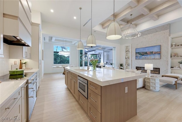 kitchen featuring open floor plan, light wood-style flooring, coffered ceiling, stainless steel appliances, and a sink