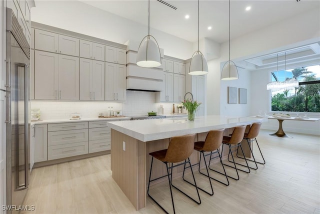 kitchen featuring a center island with sink, light countertops, light wood-style floors, a kitchen breakfast bar, and backsplash