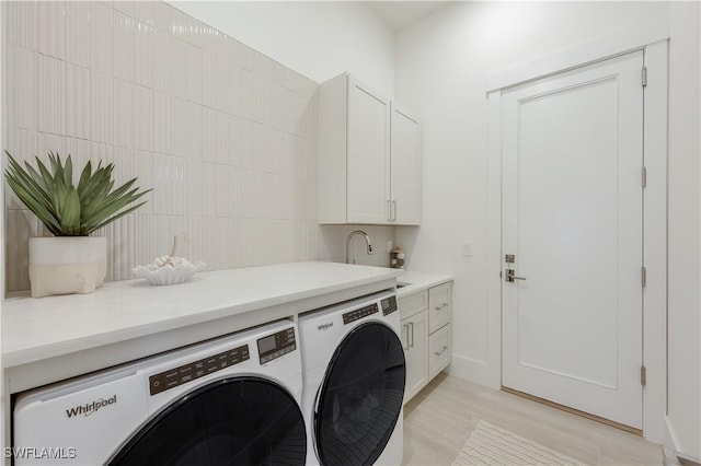 clothes washing area with cabinet space, light wood-style flooring, washing machine and dryer, and a sink