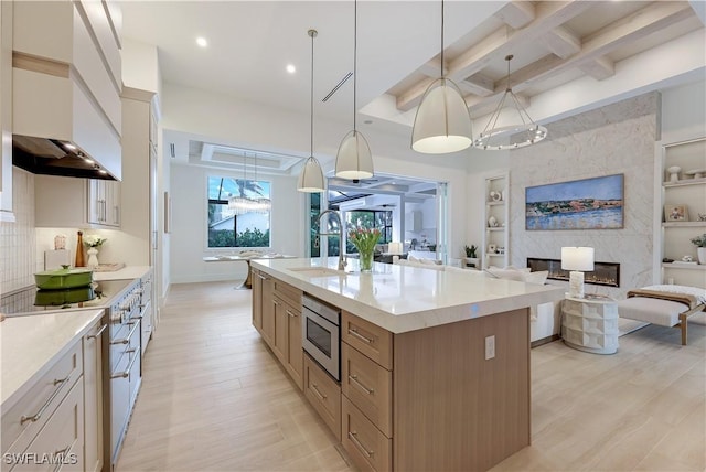 kitchen featuring open floor plan, light wood-style flooring, coffered ceiling, stainless steel appliances, and a sink