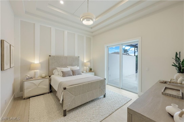 bedroom with a tray ceiling, access to outside, baseboards, and light wood finished floors