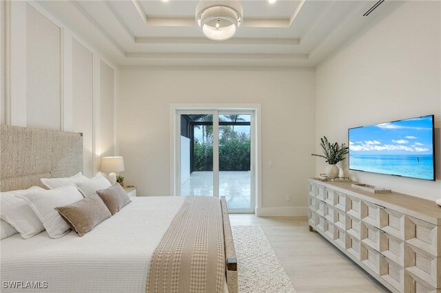 bedroom with access to exterior, a towering ceiling, light wood-style floors, and a tray ceiling