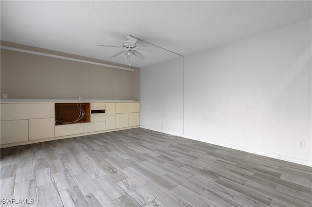 empty room featuring a textured ceiling, light wood-style floors, and a ceiling fan