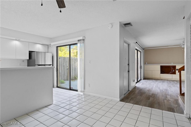 unfurnished living room with tile patterned floors, visible vents, a textured ceiling, and a ceiling fan