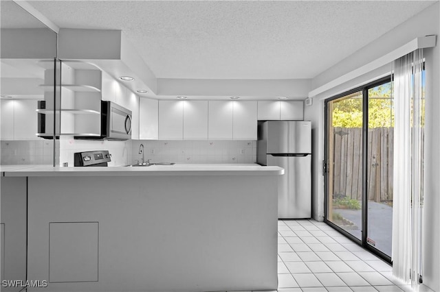 kitchen with backsplash, white cabinetry, a peninsula, stainless steel appliances, and a sink