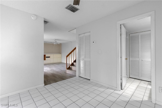 empty room with tile patterned flooring, visible vents, stairs, and a ceiling fan