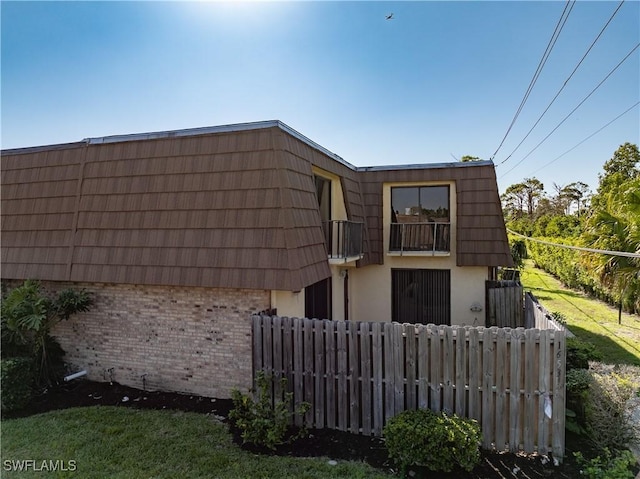 rear view of property featuring brick siding, mansard roof, and fence