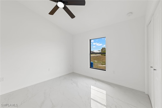 empty room with marble finish floor, a ceiling fan, baseboards, and vaulted ceiling