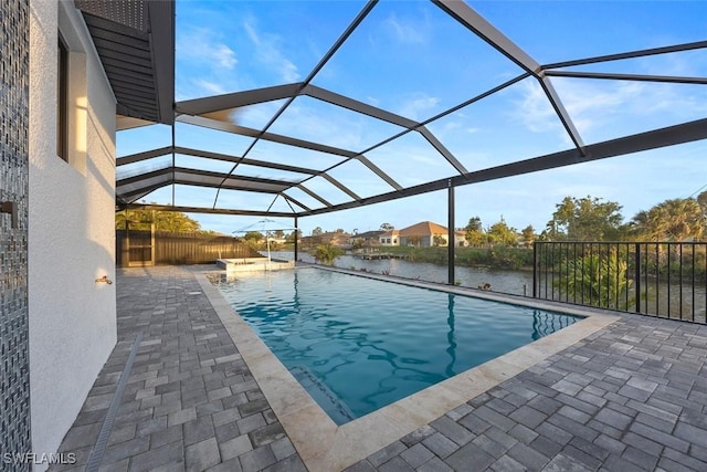 pool with a patio area, glass enclosure, and a water view