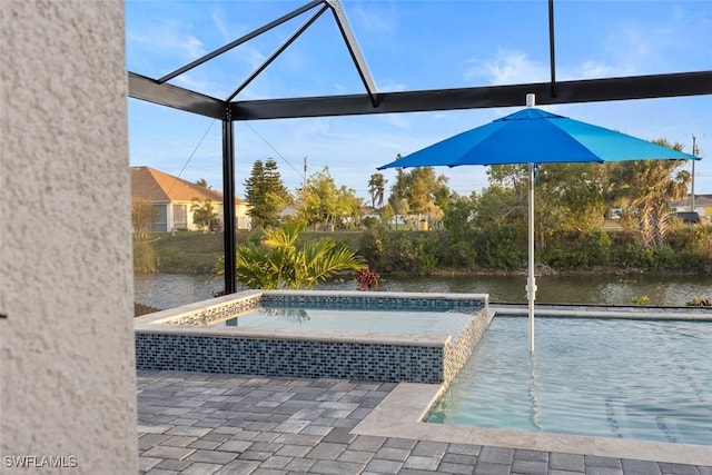 outdoor pool with a patio area, glass enclosure, an in ground hot tub, and a water view