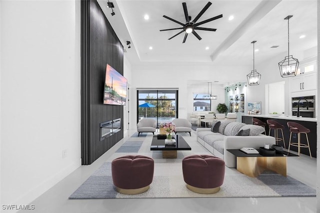 living area with a ceiling fan, concrete floors, a tray ceiling, a high ceiling, and recessed lighting