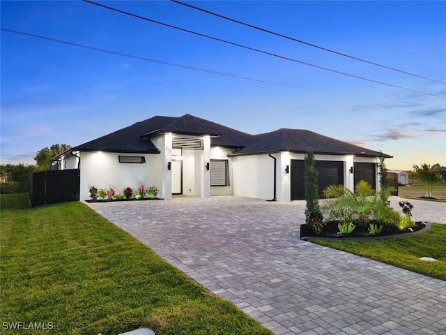 view of front of property with fence, stucco siding, decorative driveway, a yard, and a garage