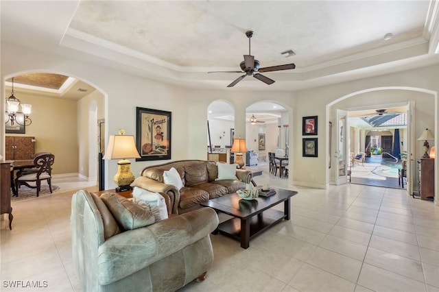 living area with a raised ceiling, arched walkways, light tile patterned floors, baseboards, and ceiling fan