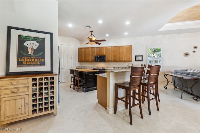 kitchen featuring a kitchen bar, a ceiling fan, visible vents, and light stone countertops