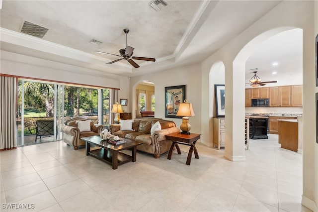 living room featuring arched walkways, visible vents, a tray ceiling, and ceiling fan