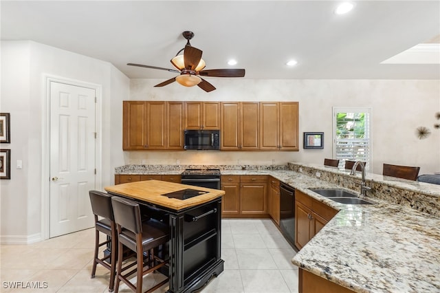 kitchen with brown cabinets, black appliances, a sink, light stone counters, and light tile patterned flooring