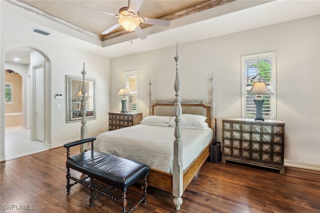 bedroom featuring wood finished floors, baseboards, visible vents, a tray ceiling, and arched walkways