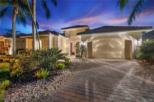 mediterranean / spanish-style house with a tiled roof, stucco siding, an attached garage, and decorative driveway