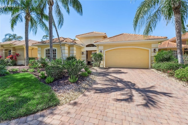 mediterranean / spanish house featuring stucco siding, decorative driveway, an attached garage, and a tiled roof