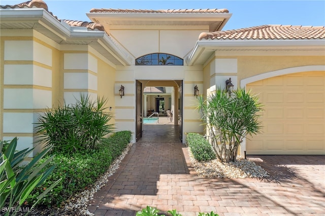 doorway to property featuring a tile roof, a garage, driveway, and stucco siding