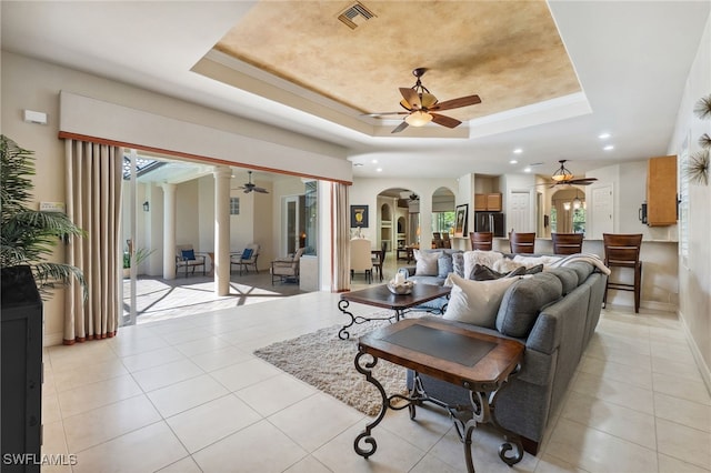 living room featuring visible vents, ceiling fan, light tile patterned flooring, arched walkways, and a raised ceiling