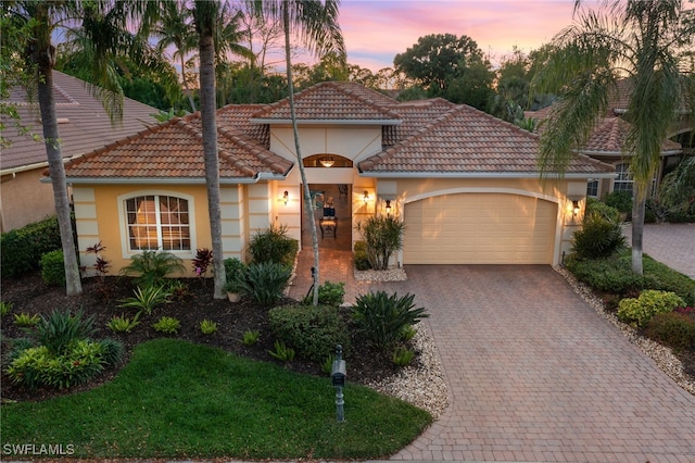 mediterranean / spanish-style house featuring stucco siding, a tiled roof, decorative driveway, and a garage