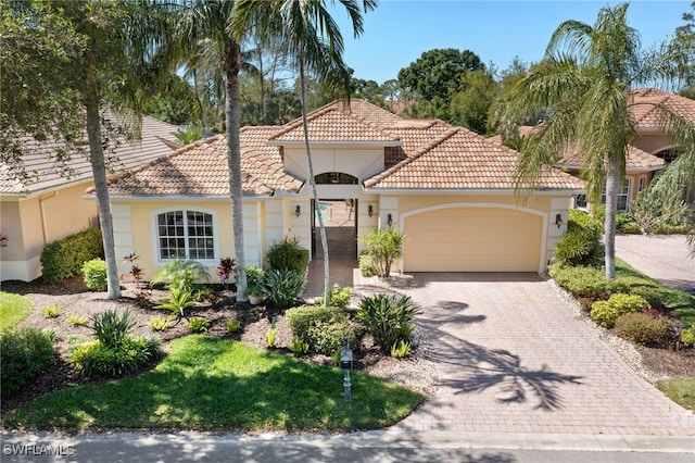 mediterranean / spanish-style home with stucco siding, driveway, an attached garage, and a tiled roof