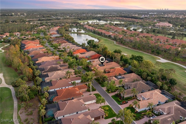 aerial view at dusk with golf course view, a water view, and a residential view