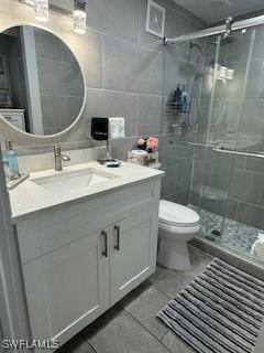 bathroom with tile patterned flooring, toilet, vanity, a stall shower, and tile walls