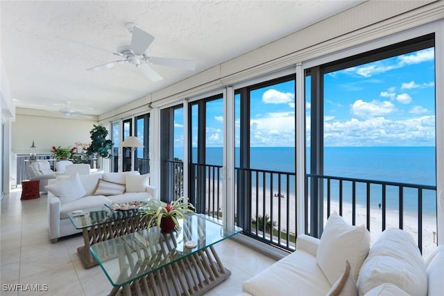 sunroom featuring a view of the beach, a water view, and ceiling fan