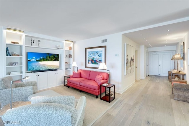 living area with visible vents, light wood-style flooring, built in shelves, and baseboards