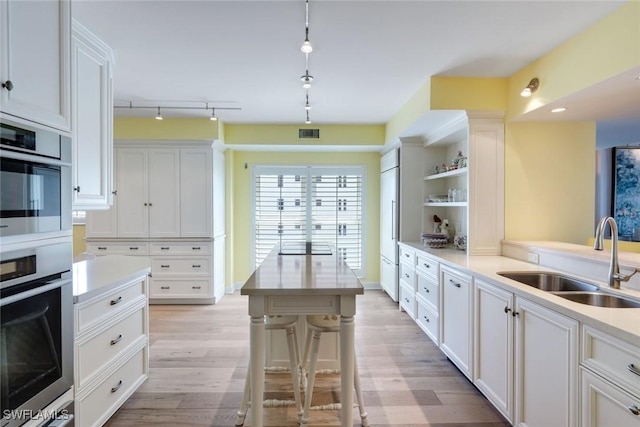 kitchen featuring a sink, open shelves, double oven, and light wood finished floors