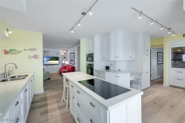 kitchen with light wood-type flooring, stainless steel oven, white cabinetry, black electric cooktop, and a sink