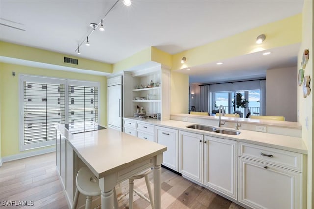 kitchen featuring open shelves, visible vents, light wood-type flooring, and a sink