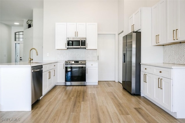 kitchen with a sink, white cabinetry, stainless steel appliances, light wood-style floors, and a peninsula