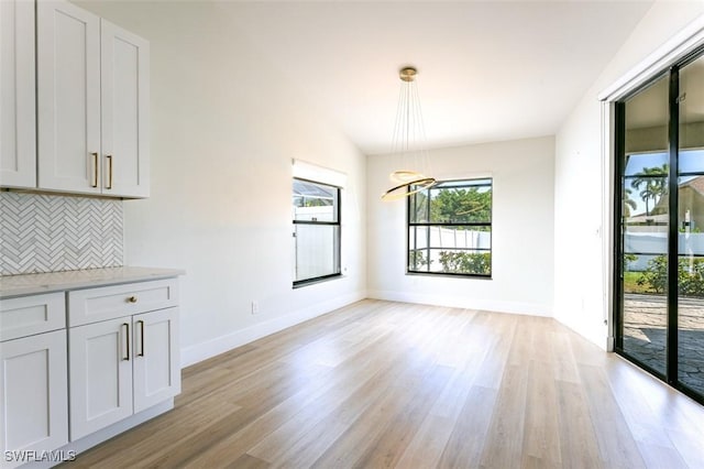 unfurnished dining area with vaulted ceiling, light wood-style flooring, baseboards, and a chandelier