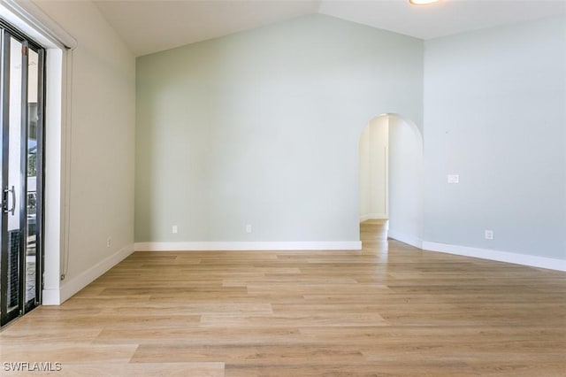 spare room featuring vaulted ceiling, light wood-style floors, arched walkways, and baseboards