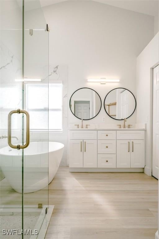 full bath featuring double vanity, wood finished floors, a freestanding bath, and a sink