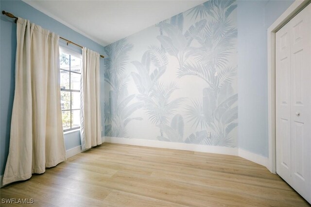 empty room with baseboards, wood finished floors, an accent wall, and wallpapered walls