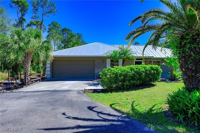 ranch-style house with concrete driveway, a front yard, stucco siding, metal roof, and an attached garage