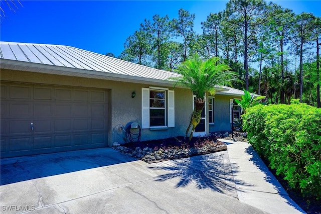 view of front of house featuring concrete driveway, stucco siding, metal roof, a garage, and a standing seam roof