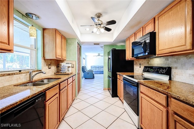 kitchen featuring black appliances, a sink, dark stone counters, a raised ceiling, and ceiling fan