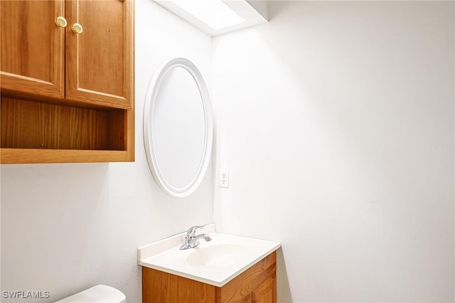 half bath featuring a skylight, toilet, and vanity