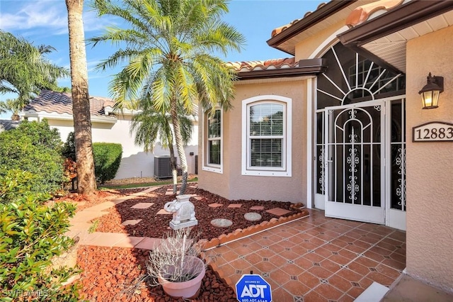 property entrance with stucco siding, cooling unit, and a tiled roof