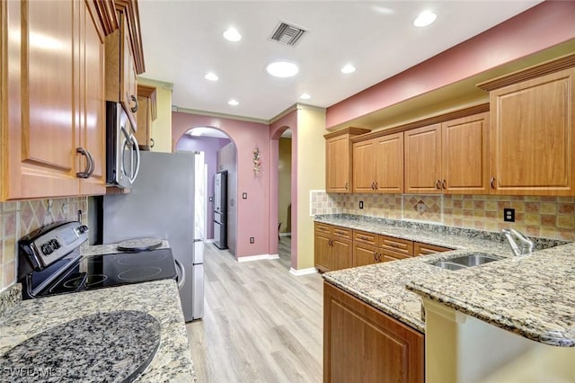 kitchen featuring visible vents, a sink, light stone counters, stainless steel appliances, and arched walkways