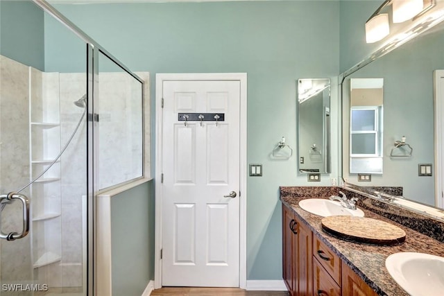 bathroom featuring a sink, baseboards, double vanity, and a shower stall