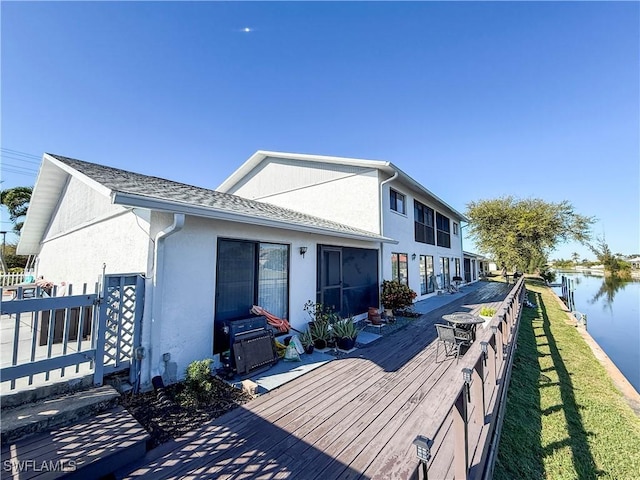 rear view of property with fence, a deck with water view, roof with shingles, and stucco siding