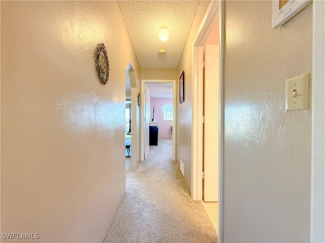 hall with a textured wall, visible vents, light colored carpet, and a textured ceiling